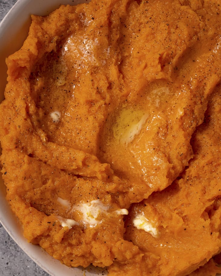A photo of a closeup of mashed butternut squash in a white bowl with melted butter on top.
