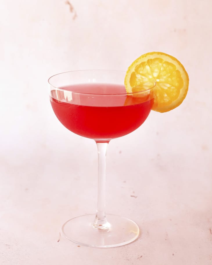 A photo of a bright red cosmopolitan cocktail with a lemon wedge on the side of the cocktail glass.