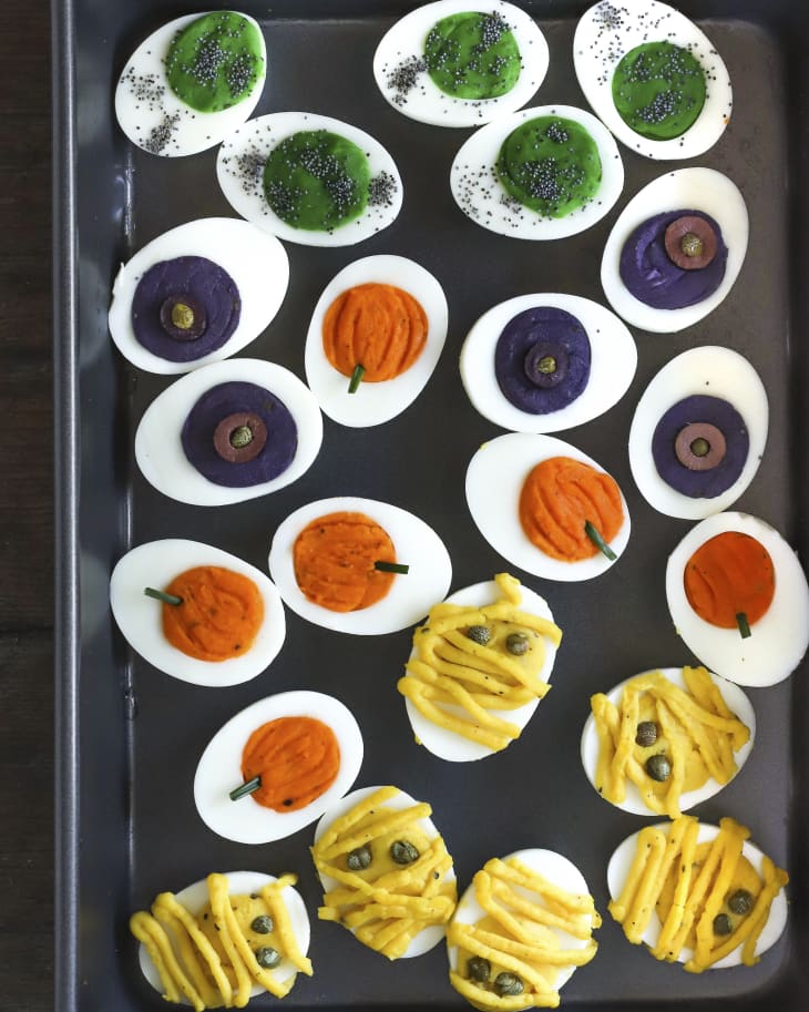 A photo of a rectangular platter of deviled eggs, with the yolk filling made into different colors with various halloween figures such as pumpkin and mummies.