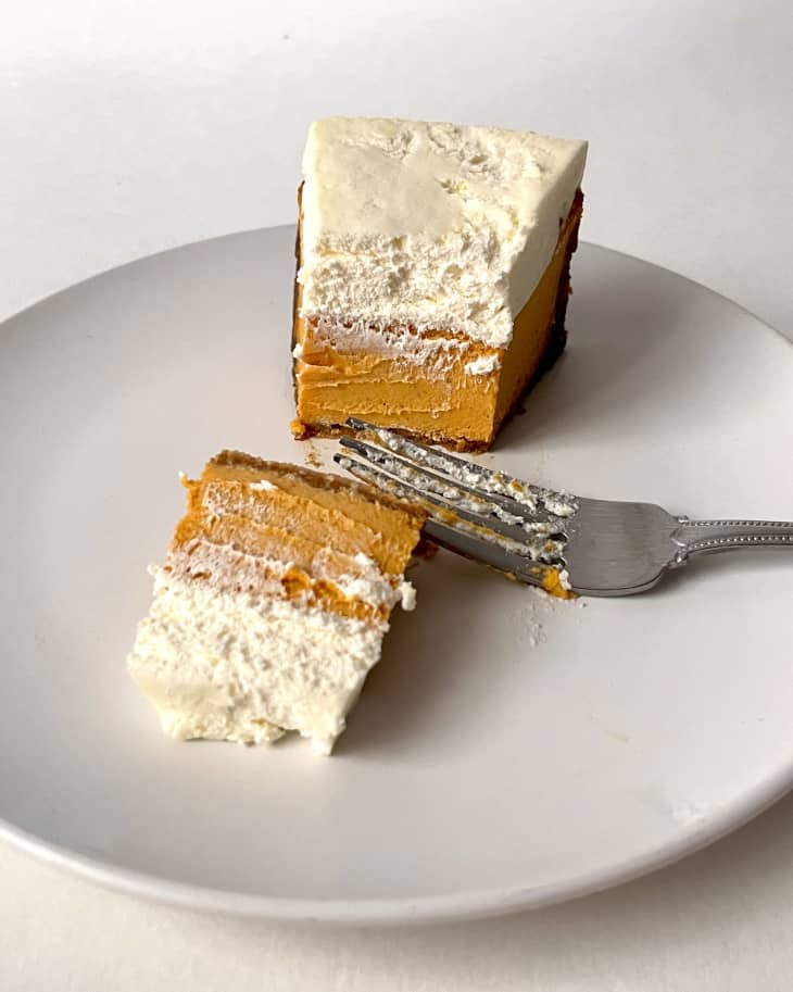 A photo of a slice of sweet potato cheesecake on a plate, cut in half with a fork on the plate.