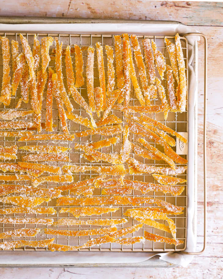 A photo of strips of candied orange peel dusted with sugar on a wire cooling rack.