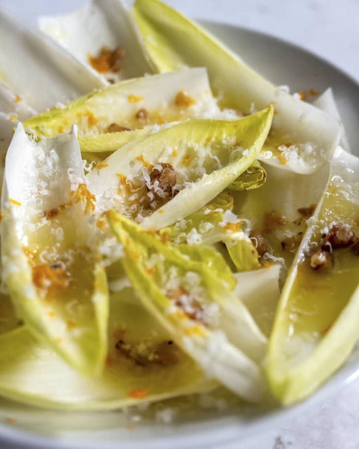 A photo of an endive salad with crushed nuts and shaved cheese on top.