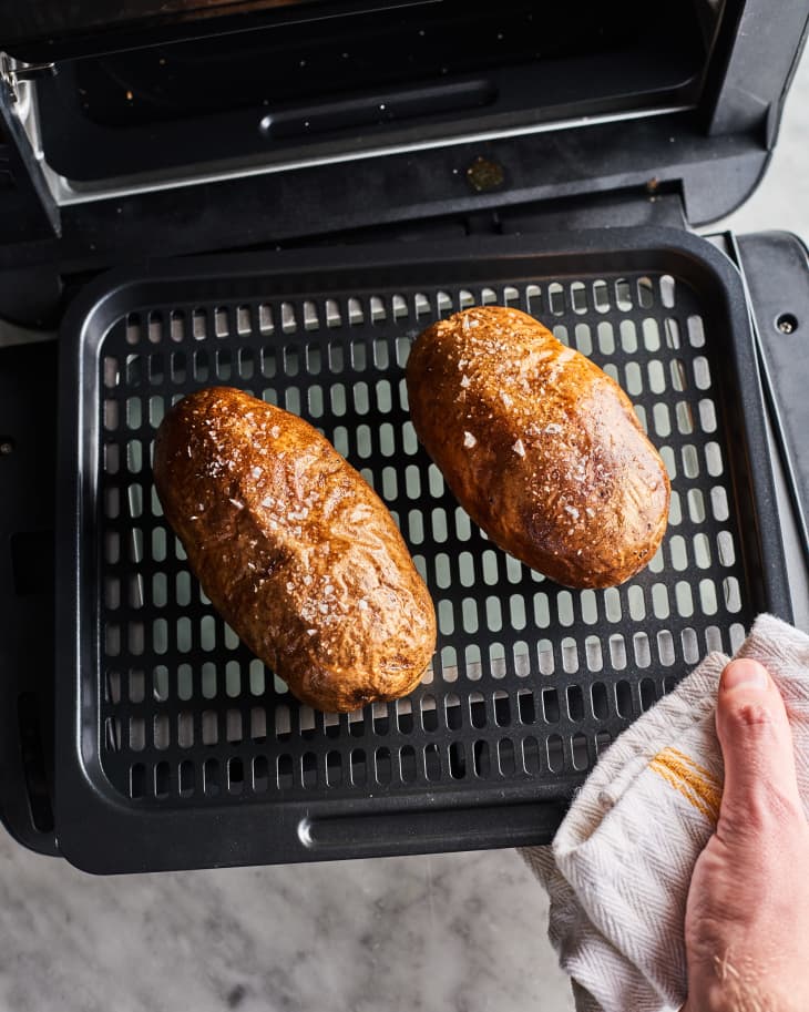 pulling 2 baked potatoes out of an air fryer