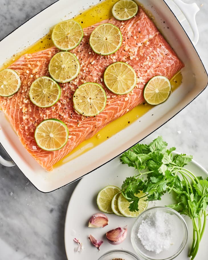 Salmon marinading in a roasting pan with limes and a plate of ingredients on the side