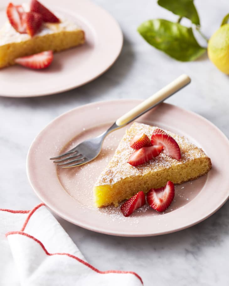 Slice of flourless lemon almond cake lightly topped with powered sugar and quartered strawberries