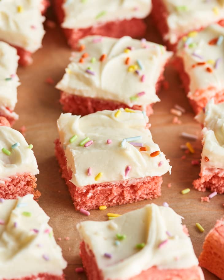 Closeup of pink strawberry brownie squares topped with vanilla frosting and sprinkles