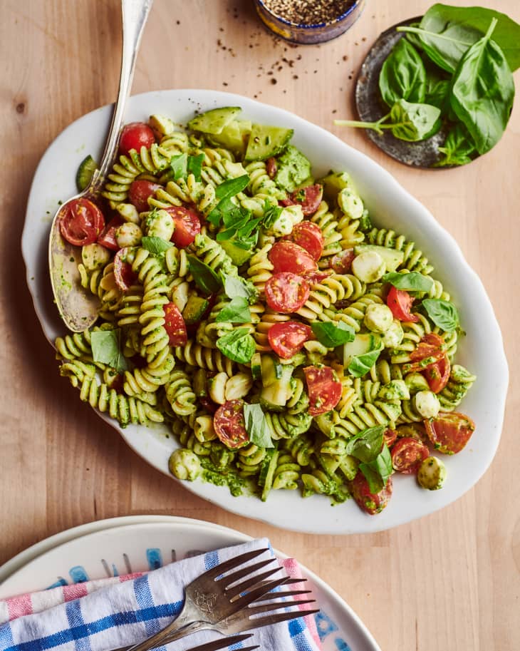 Platter of pesto pasta salad with plates, forks, and napkins