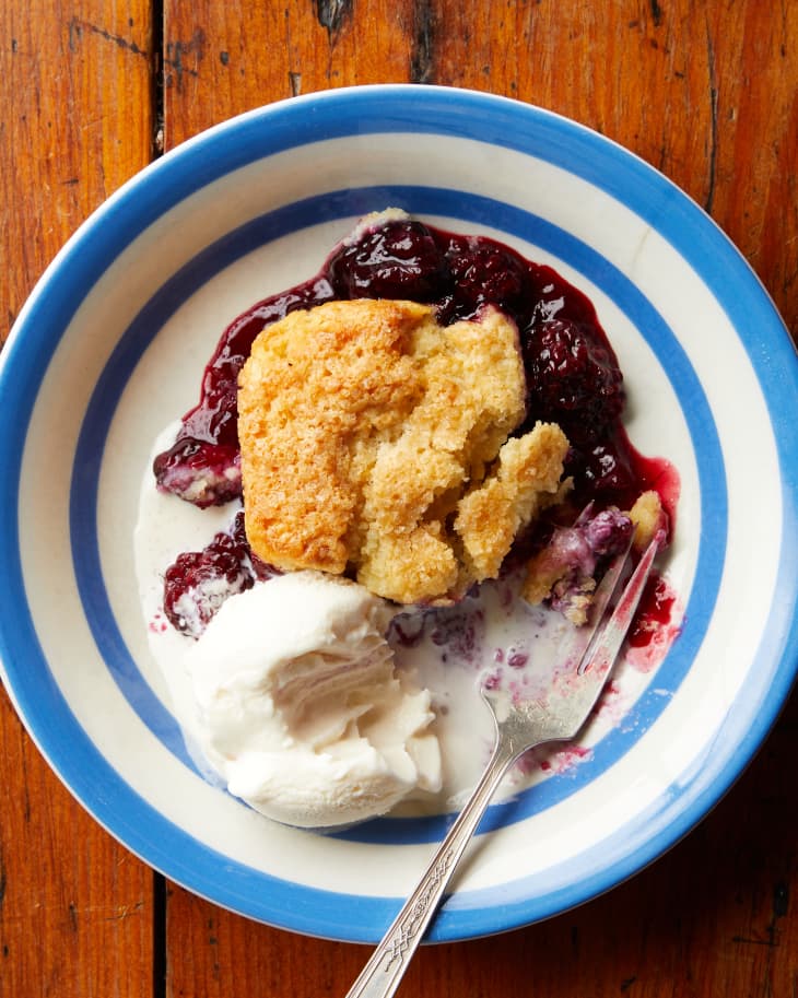 A single serving of berry cobbler sits on a plate next to vanilla ice cream.