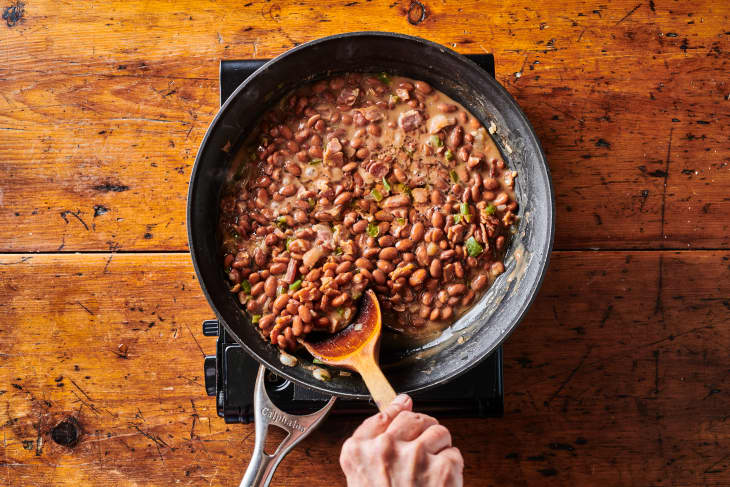 Wooden spoon stirring pinto beans in skillet