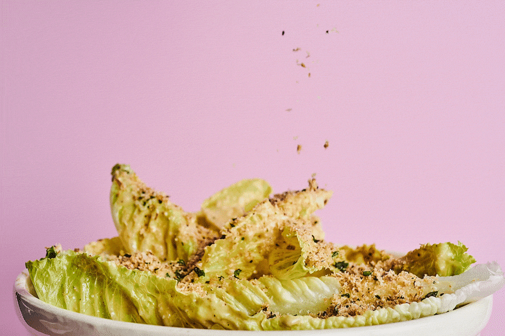 Breadcrumbs rain down over a bed of romaine leaves covered in caesar salad dressing.