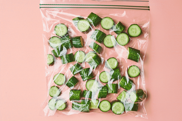 A plastic bag full of cut up cucumber is hit with a  wood rolling block in order to smash the cucumbers.