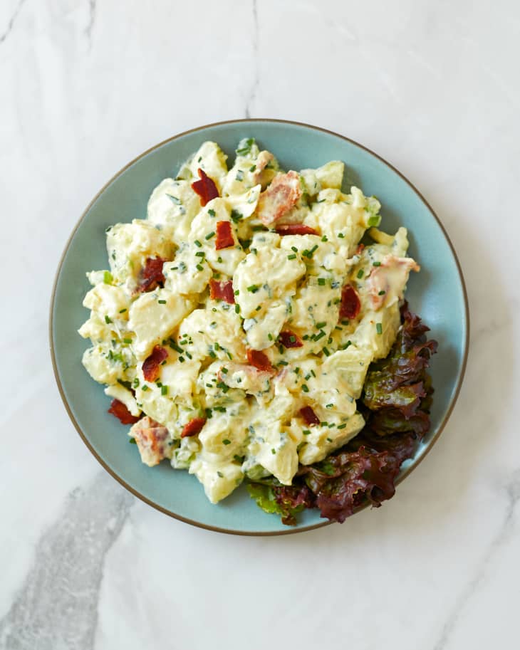 Julia Child's potato salad with bacon and chives on a bed of purple romaine lettuce placed on a light blue ceramic plate