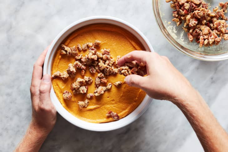 Someone topping sweet potato souffle with pecans.