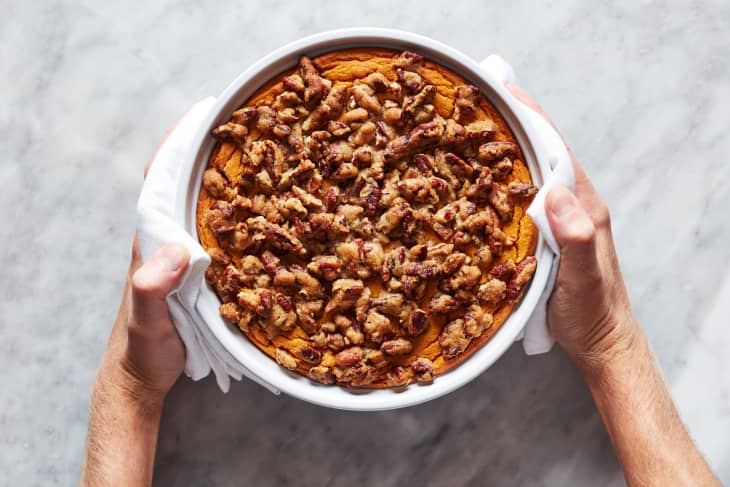 Someone holding dish of sweet potato souffle topped with pecans.