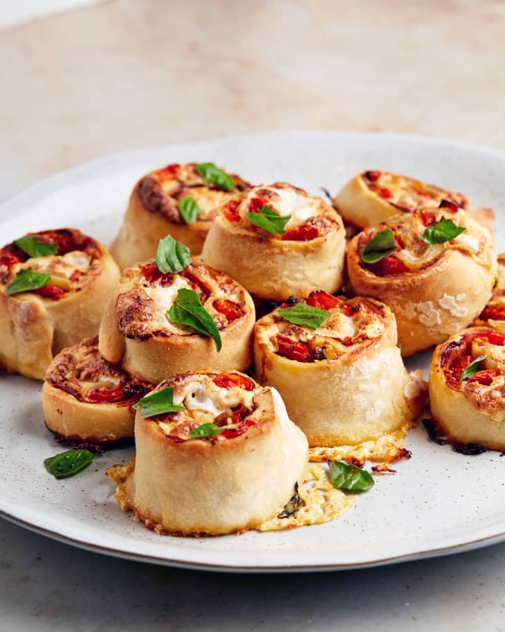 Fancy pizza rolls garnished with basil; stacked on a plate.