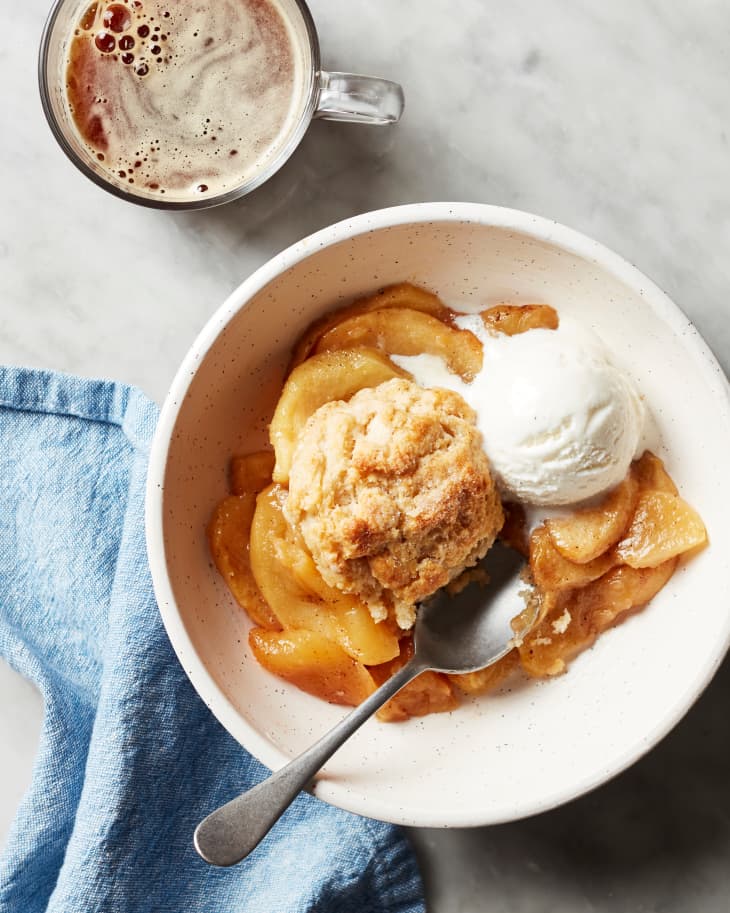 Easy apple cobbler in white bowl with scoop of ice cream on top and spoon on side.