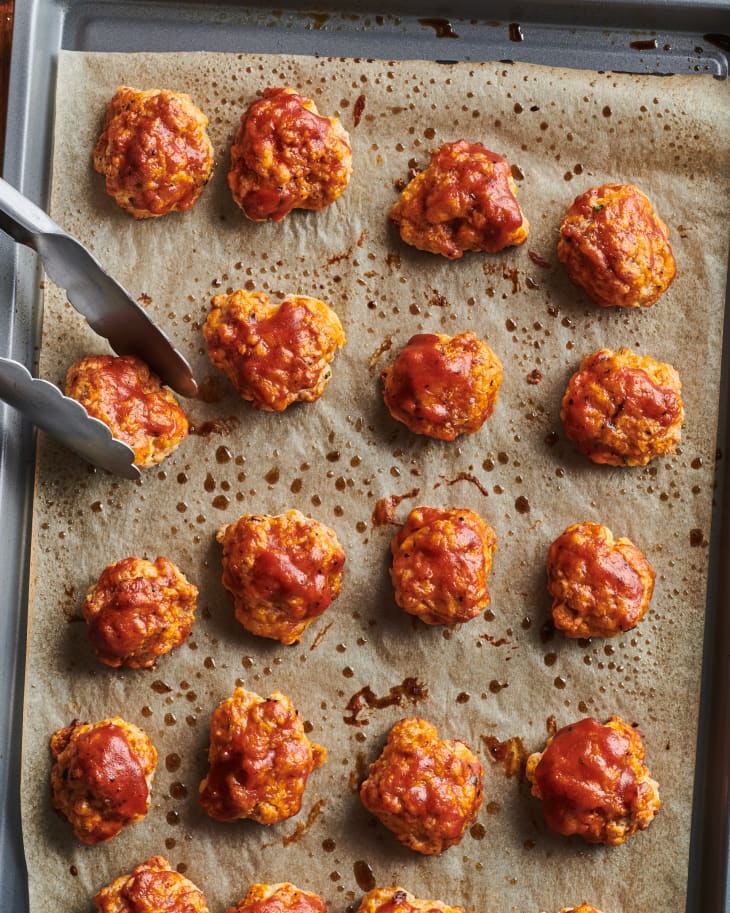Sausage balls on baking sheet being picked up with tongs.