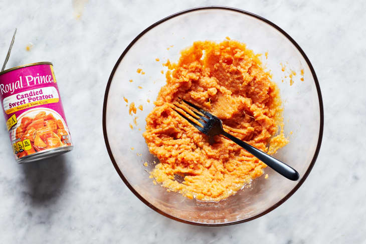 Smashed candied sweet potato in glass bowl with fork resting inside.