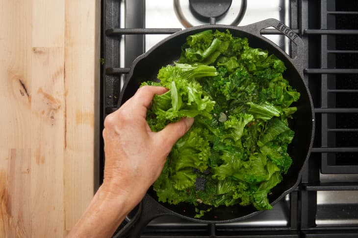 Mustard greens being added to cast iron skillet.