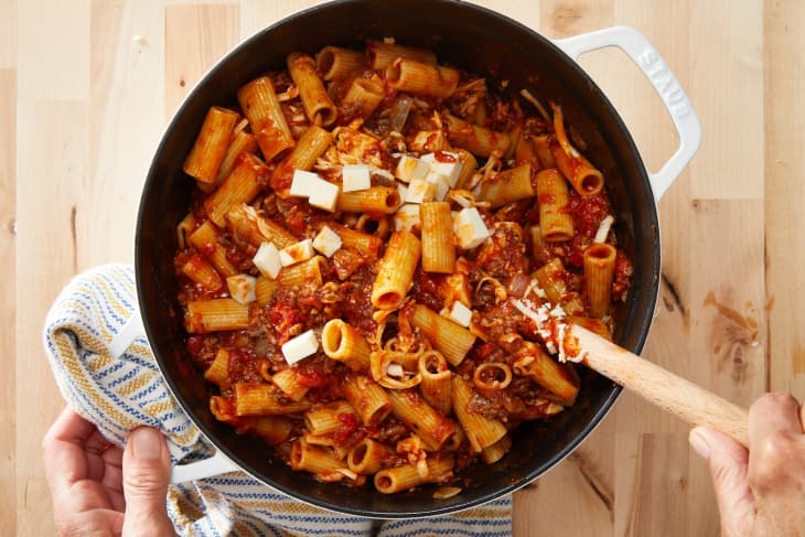 Someone mixing cheesy rigatoni and beef mixture in large pot with wooden spoon.