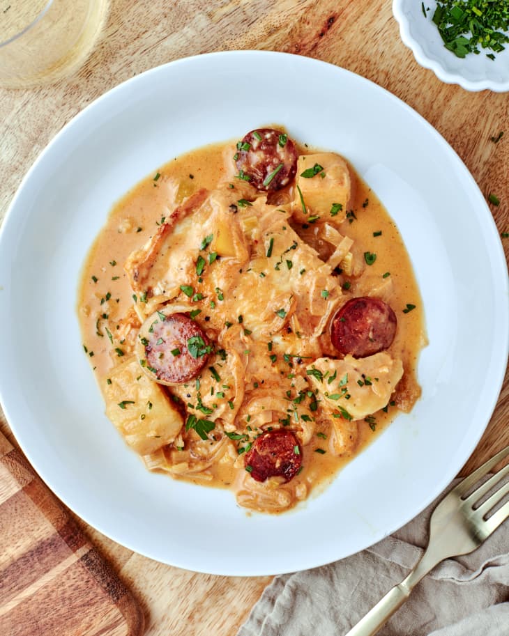 one plate of creamy chicken with chorizo and potatoes sits near a fork on a wooden table