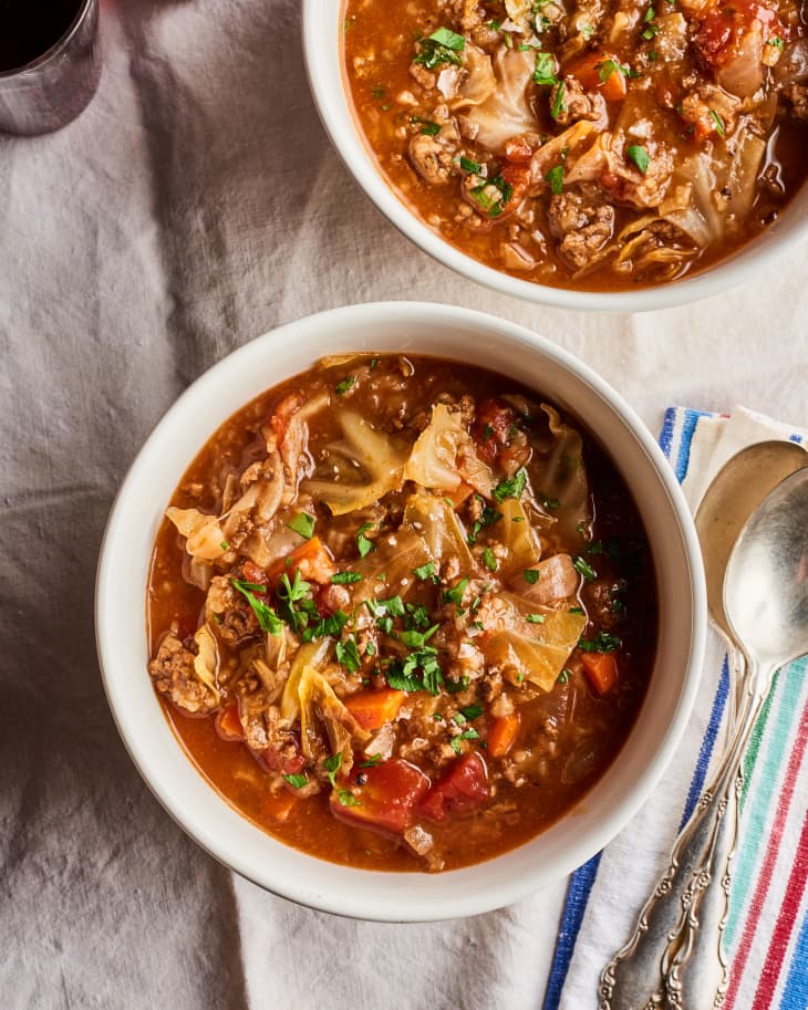 cabbage roll soup in a bowl sits on top of a white linen and near a striped napkin