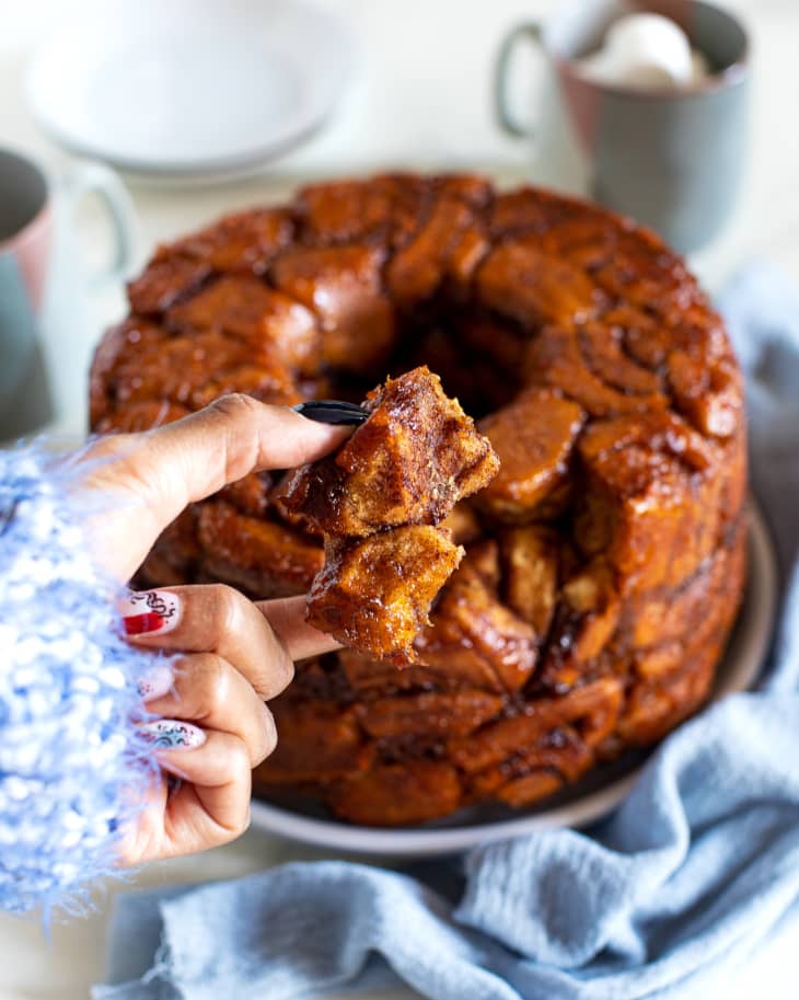 someone is pulling monkey bread from finished bread on a white plate on a blue napkin