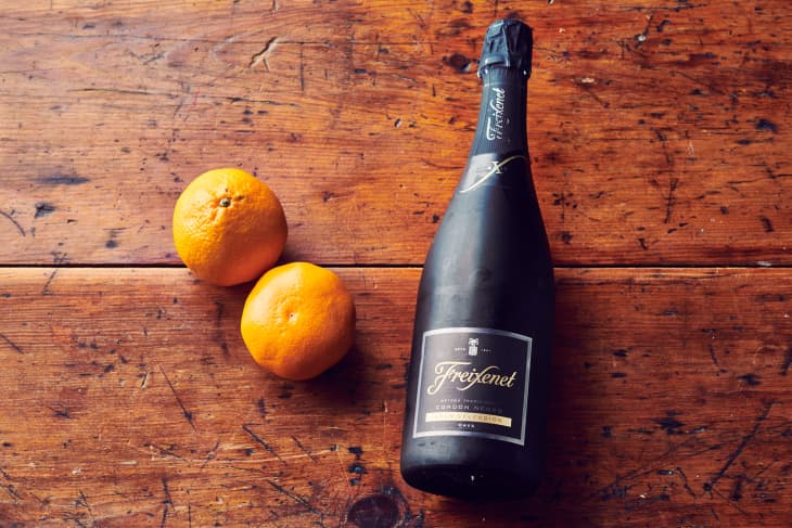 Two tangerines and a bottle of Freixenet Cava sit on a wooden table.