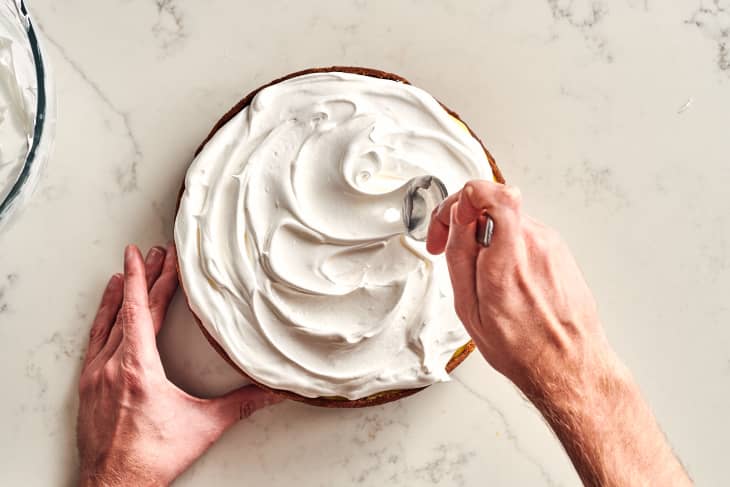 someone applying cream to the top of the lemon meringue cheesecake