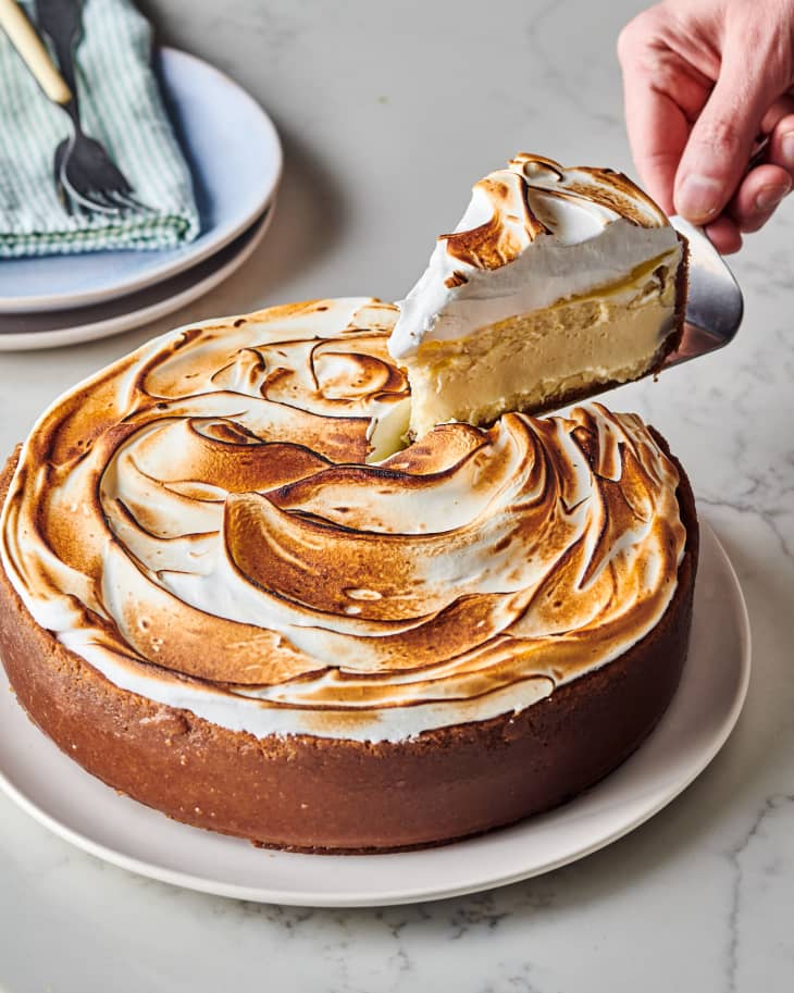 full finished lemon meringue cheesecake with someone taking a slice out with a metal cake utensil