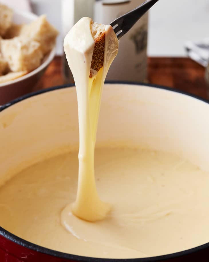 someone is dipping a piece of bread in the fondue, with the cheese dripping off