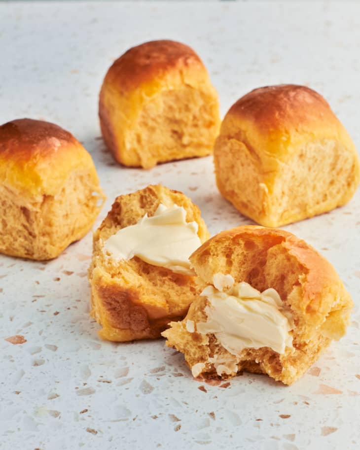 dinner rolls sit on the table with one cut in half and buttered