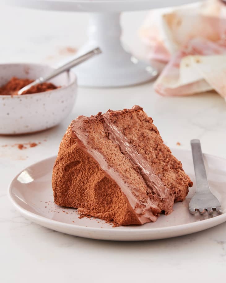 a slice of angel food dream cake sits on a plate on a table near a bowl of cocoa powder