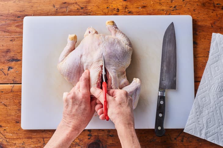 someone is cutting a raw skinned chicken with scissors