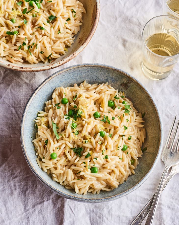 orzo sits in a bowl next to a glass of wine on a table ready to eat