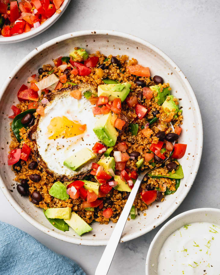 Smoky Quinoa Bowls with Avocado and Fried Eggs sits on a table with a fork in it ready to eat