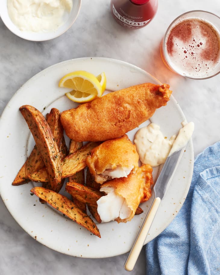 beer battered fish sits with french fried and lemons on a plate