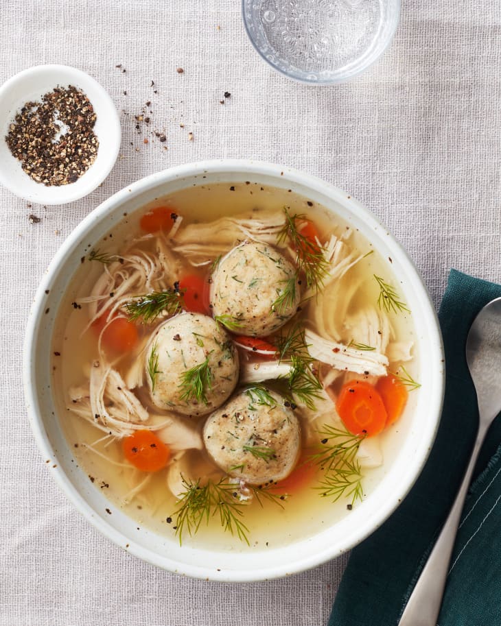 matzo ball soup sits with cutlery and a glass of water near it