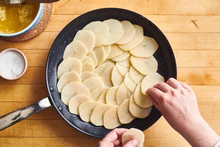 someone is layering potato slices in a pan