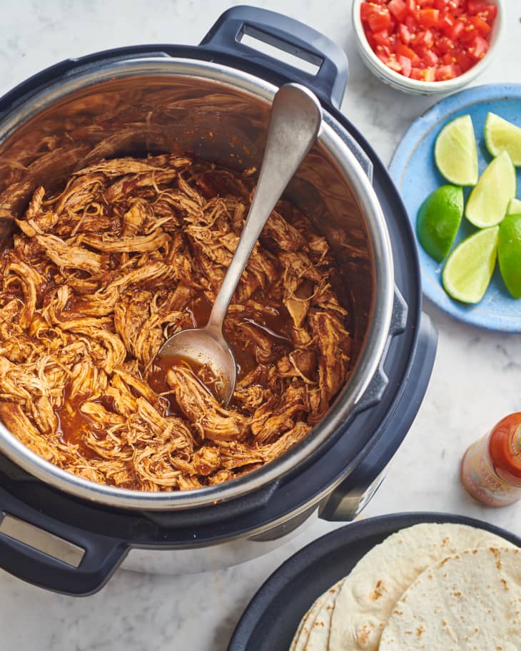 chicken sits in instant pot next to plates of tortillas and limes