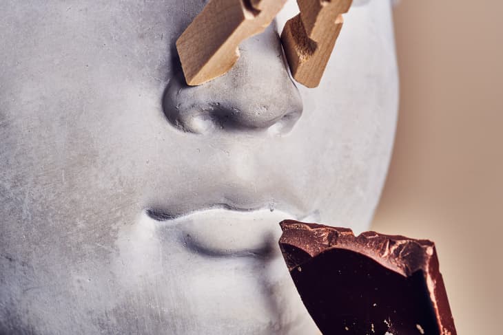chocolate being held to a busts mouth with a clothespin on its nose