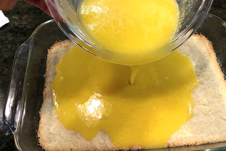 lemon bars in a baking dish with lemon being poured in