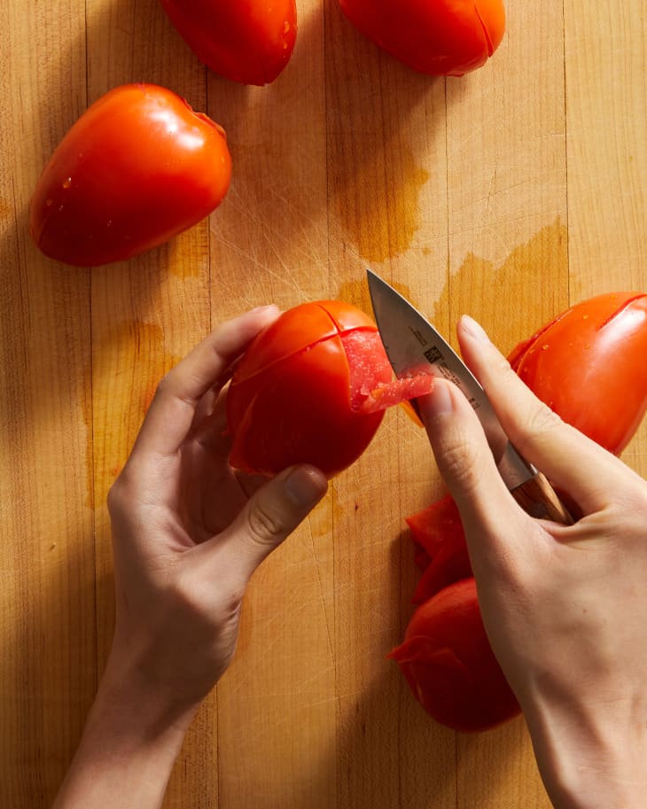 someone peeling a tomato with a knife