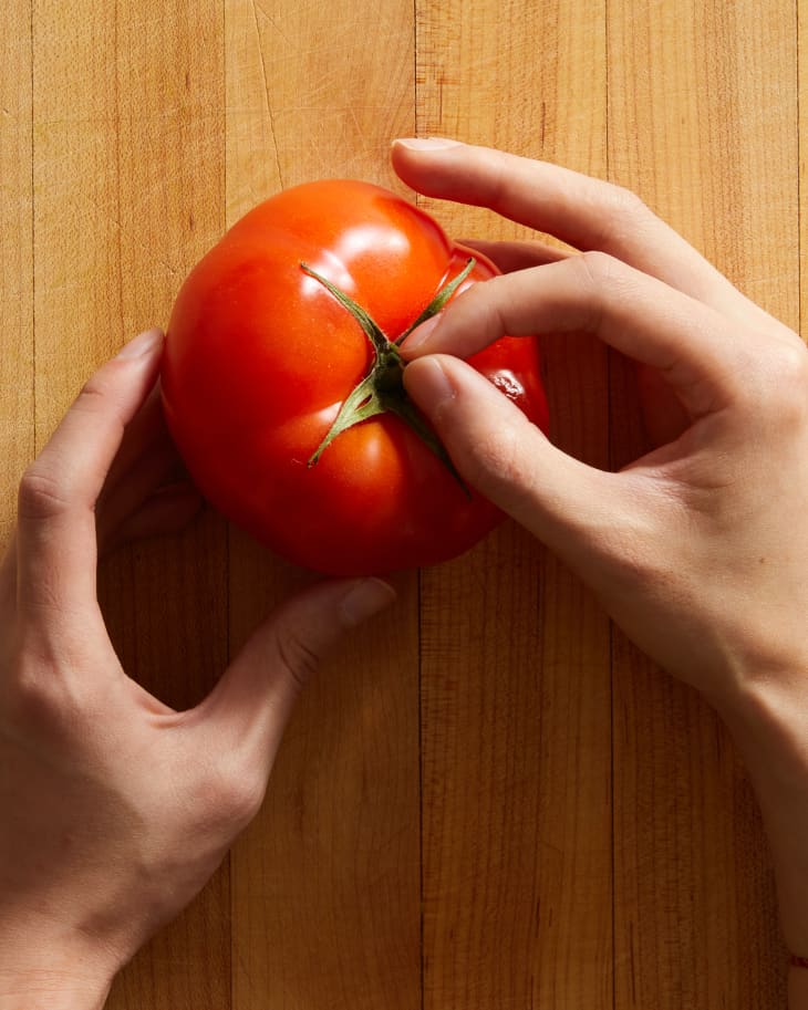 someone pulling the stem of tomato