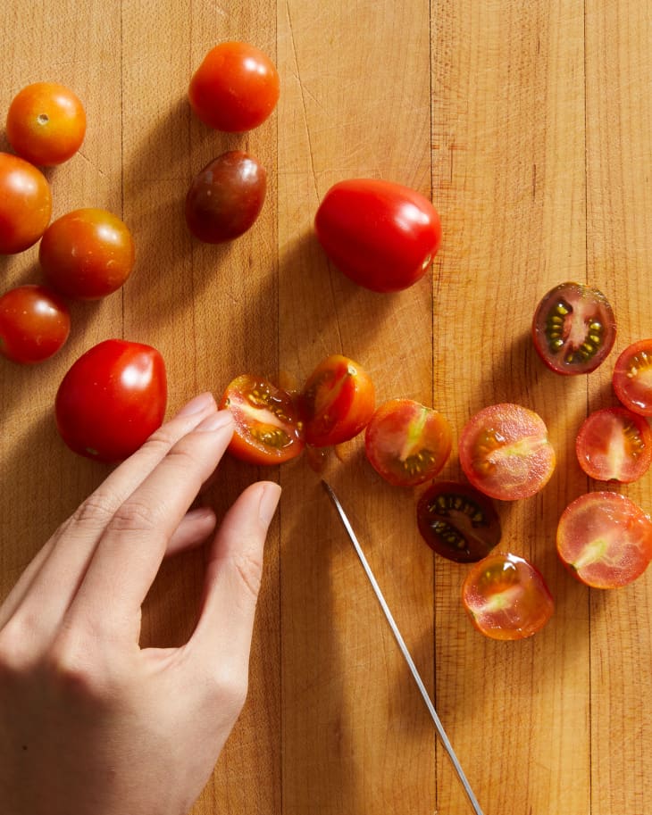 someone slicing cherry tomatoes on cutting board