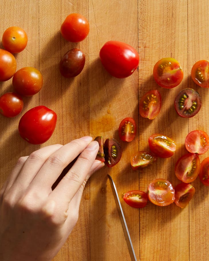 someone slicing cherry tomatoes on cutting board