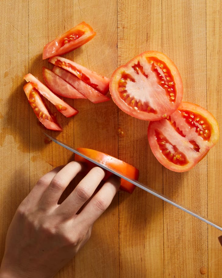 someone dicing tomatoes on a surface with their hand holding tomato