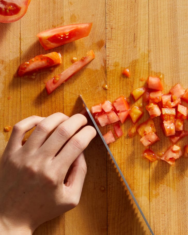 someone dicing tomatoes on a surface with their hand holding tomato