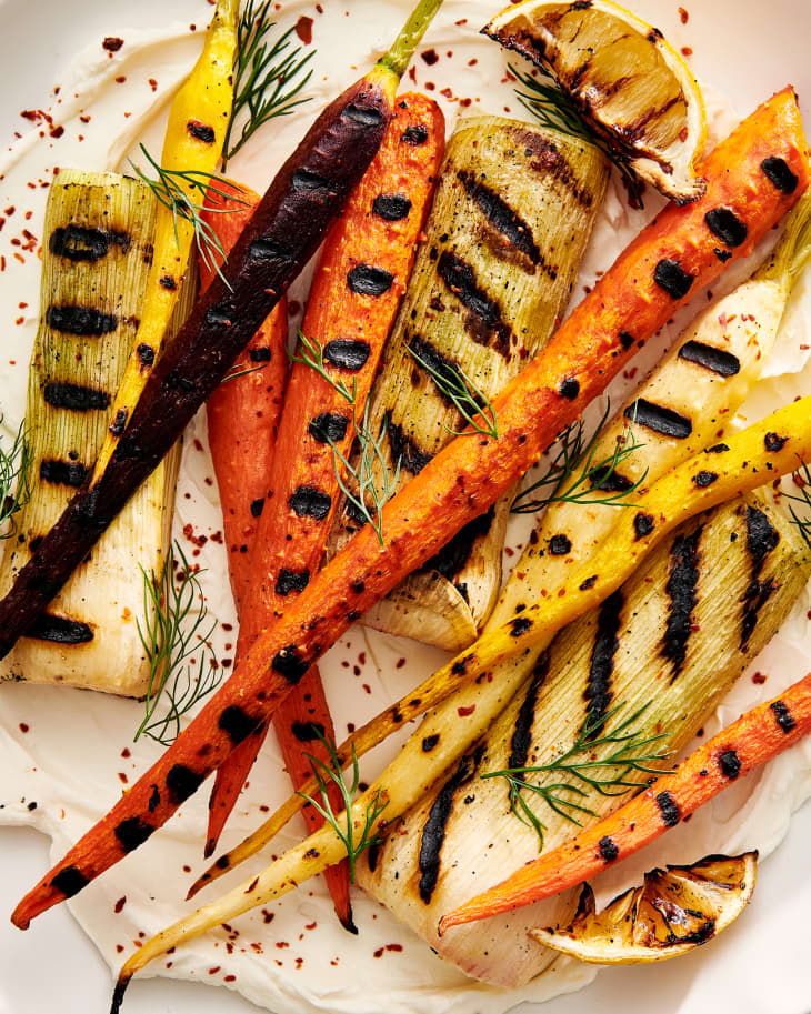 Close up of grilled yellow and orange carrots on a plate of labneh with herbs