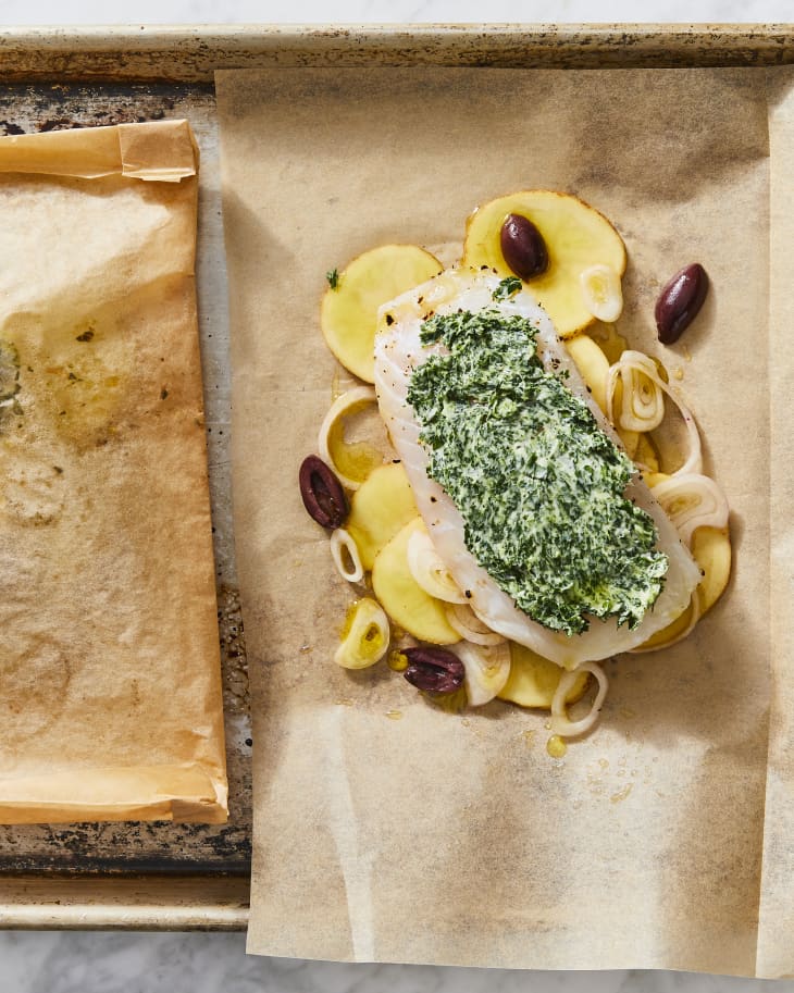 a filet of cod over potatoes with herb butter on parchment in sheet pan ready for baking